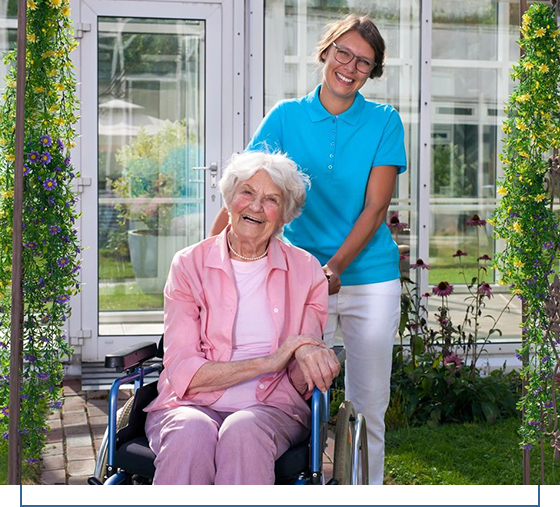 A woman standing next to an older lady in a wheelchair.